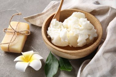 Sabun barlı bir kase Shea yağı ve gri arka planda bir çiçek.