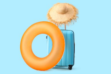 Şişme yüzük, bavul ve mavi arka planda hasır şapka. Seyahat kavramı
