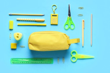 Mavi arka planda farklı kırtasiye malzemesi olan sarı kalem kutusu. Üst görünüm