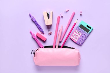 Leylak arka planında farklı kırtasiye malzemesi olan pembe kalem kutusu. Üst görünüm