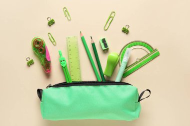 Bej arka planda farklı kırtasiye malzemesi olan yeşil kalem kutusu. Üst görünüm