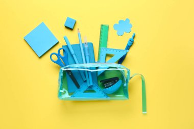 Sarı arka planda farklı kırtasiye malzemesi olan mavi kalem kutusu. Üst görünüm