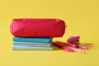 Sarı zemin üzerinde farklı kırtasiye malzemesi olan pembe kalem kutusu.