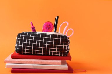 Turuncu zemin üzerinde farklı kırtasiye malzemesi olan siyah kareli kalem kutusu