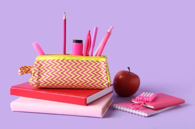 Farklı kırtasiye malzemesi ve leylak arkaplanlı elma içeren kalem kutusu