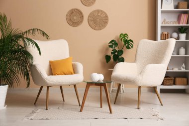 Oturma odasının içinde beyaz koltuklar, raf ünitesi, kahve masası ve ev bitkileri.