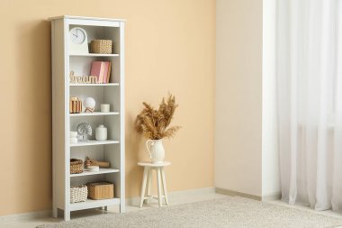 Kitaplar, vazolar ve sepetlerle raflar oturma odasındaki bej duvarın yanında.