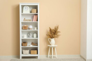 Kitaplar, vazolar ve sepetlerle raflar oturma odasındaki bej duvarın yanında.