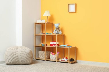 Lamba, çocuk oyuncakları ve puf sarı duvarın yanında.