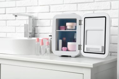 Lavabo, kozmetik buzdolabı, beyaz tuğla duvarın yanında şişeler ve kozmetik ürünler.