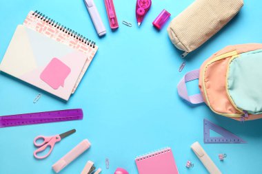 Mavi arka planda sırt çantalı okul malzemelerinden yapılmış çerçeve. Üst görünüm