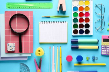 Mavi arka planda büyüteç olan okul malzemeleri. Üst görünüm
