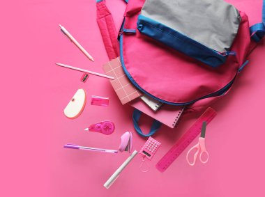 Kitaplar ve sırt çantaları pembe arka planda farklı okul kırtasiyeleriyle uçuyor.