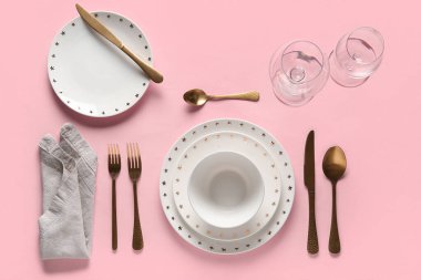 Pembe arka planda altın çatal bıçak takımı olan güzel bir masa.