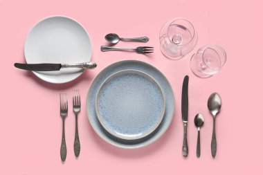 Pembe arka planda gümüş çatal bıçak seti olan güzel bir masa.