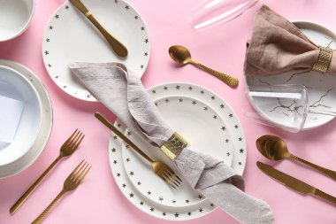 Pembe arka planda altın çatal bıçak ve peçeteyle güzel bir masa.