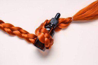 Kırmızı saç örgüsü ve kozmetik ürünler hafif arka planda, yakın plan.