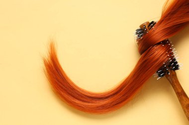 Yuvarlak saç fırçası, soluk sarı arka planda kırmızı saç teli.