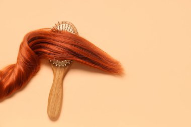 Kırmızı saç teli ve bej arka planda saç fırçası.