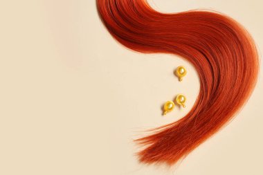 Kırmızı saç teli ve bej arka planda kapsüller