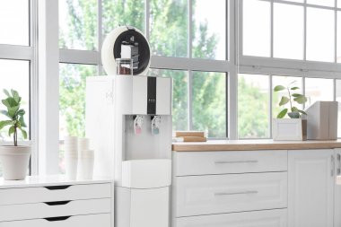 Ofisinde pencere kenarında kahve makinesi olan modern su soğutucusu.