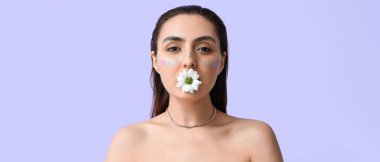 Yaratıcı makyajlı güzel bir kadın leylak arka planında papatya çiçeğini tutuyor.