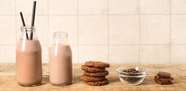 Çikolatalı süt şişeleri ve ahşap masada lezzetli kurabiyeler.