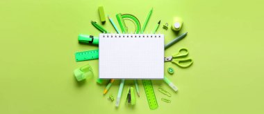 Yeşil arka planda farklı okul malzemeleri, üst manzara.