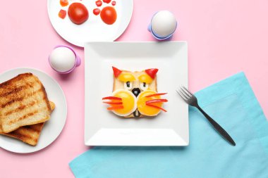 Pembe arka planda kedi, tost ve sebze şeklinde komik bir kahvaltı tabağı.