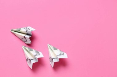 Pembe arka planda dolar banknotlarından yapılmış Origami uçakları