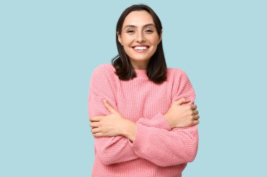 Mavi arka planda kendine sarılan genç bir kadın.