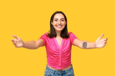 Sarı arka planda sarılmak için kollarını açan genç kadın.