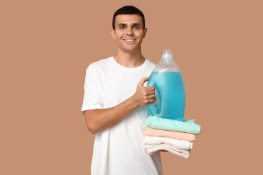Temiz havluları ve bej arka planda bir şişe deterjanı olan genç bir adam.