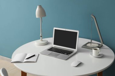 Modern dizüstü bilgisayarı, not defteri ve renkli duvarın yanında bir fincan kahvesi olan şık bir iş yeri.