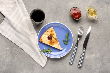 Gri grunge arka planda lezzetli pizza, çatal bıçak takımı ve peçeteyle dolu bir tabak.