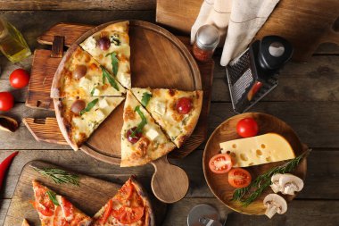 Lezzetli pizzalı tahtalar, mutfak aletleri ve ahşap arka planda malzemeler.