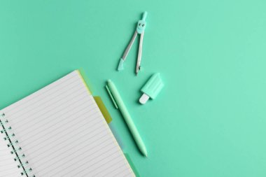 Yeşil arka planda açık defter, pusula, silgi ve kalemle kompozisyon. Üst görünüm