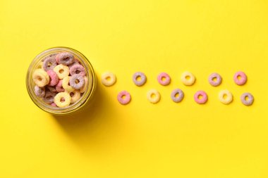 Sarı arka planda renkli tatlı mısır gevreği halkaları olan kavanoz.