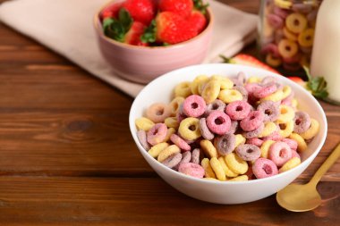 Rengarenk mısır gevreği halkaları ve ahşap arka planda çilekleri olan bir kase.