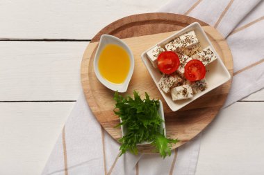 Beyaz ahşap zemin üzerinde beyaz peynir, kiraz domates, marul ve yağ dolu bir kase.