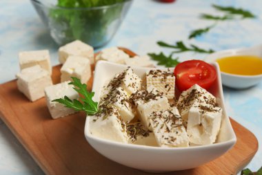 Açık mavi arkaplanda beyaz peynir, baharat, roka ve vişneli domates kasesi.