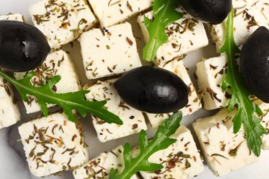 Baharatlı, siyah zeytinli ve roka arkaplanlı nefis peynir parçaları.