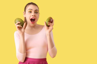 Şok olmuş genç bir kadın sarı arka planda tatlı mango meyveleriyle