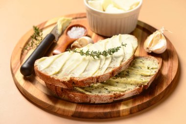 Tahta tahta ekmek dilimleri, taze tereyağı, sarımsak ve kahverengi arka planda tuz.