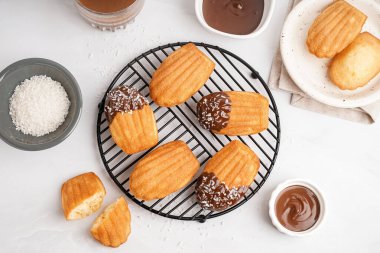 Lezzetli madeleineler, çikolata kreması kaseleri ve beyaz arka planda hindistan cevizi taneleri.