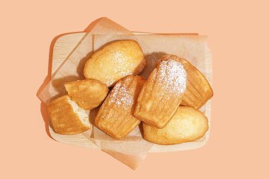 Lezzetli madeleine ve turuncu arka planda pudra şekerli ahşap tahta.