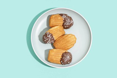 Turkuaz arka planda çikolata ve hindistan cevizi taneli lezzetli madeleine tabağı.