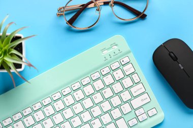 Gözlük, sulu, bilgisayar faresi ve mavi arka planda klavye. Üst görünüm