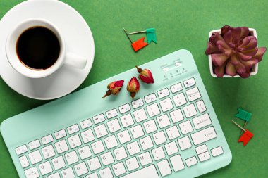 Sulu bilgisayar klavyesi, yeşil arka planda bir fincan kahve ve çiçek tomurcukları. Üst görünüm
