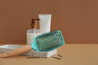 Kahverengi arka planda kozmetik ürünleri şişeleriyle saç fırçası